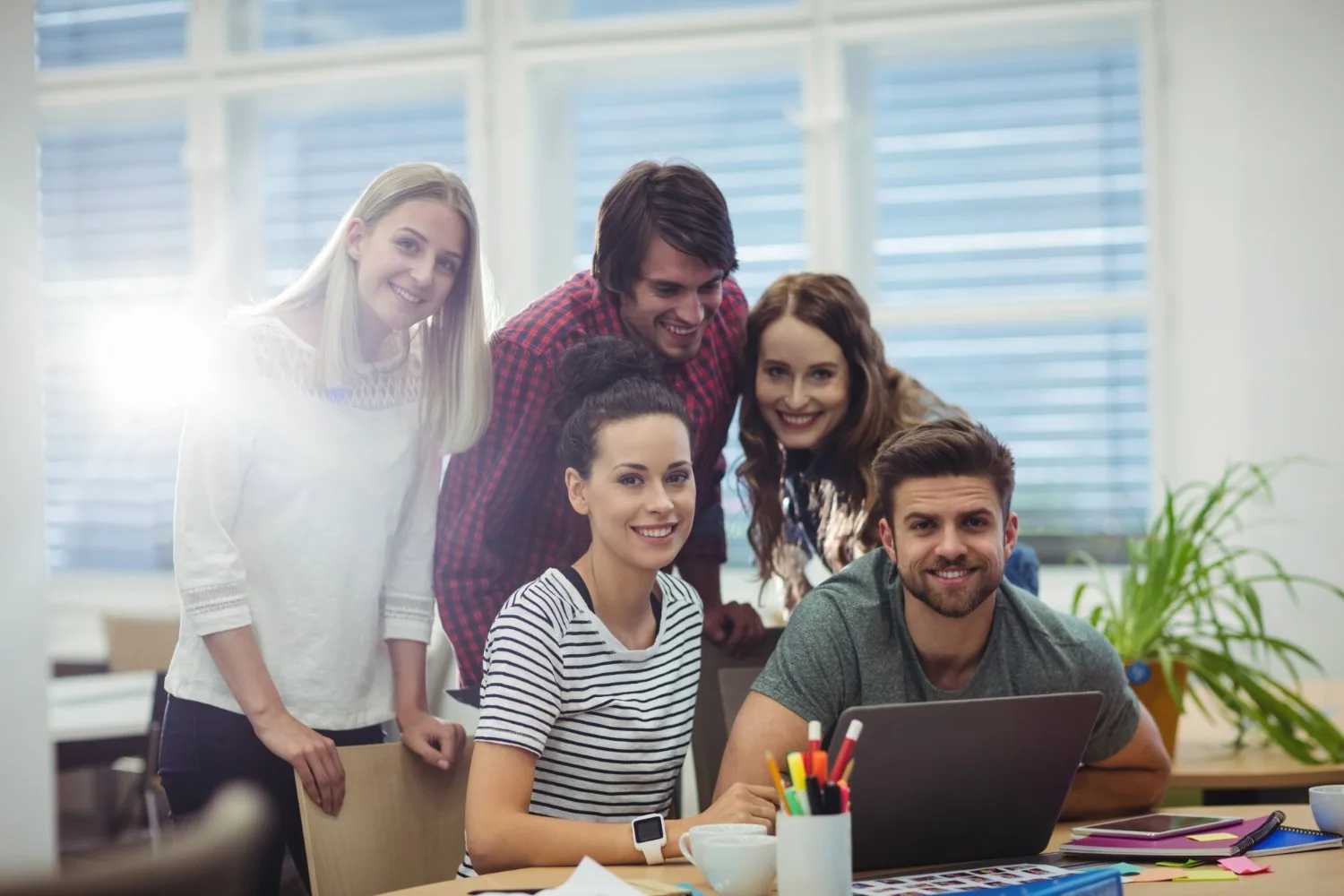 A smiling team gathered around a laptop